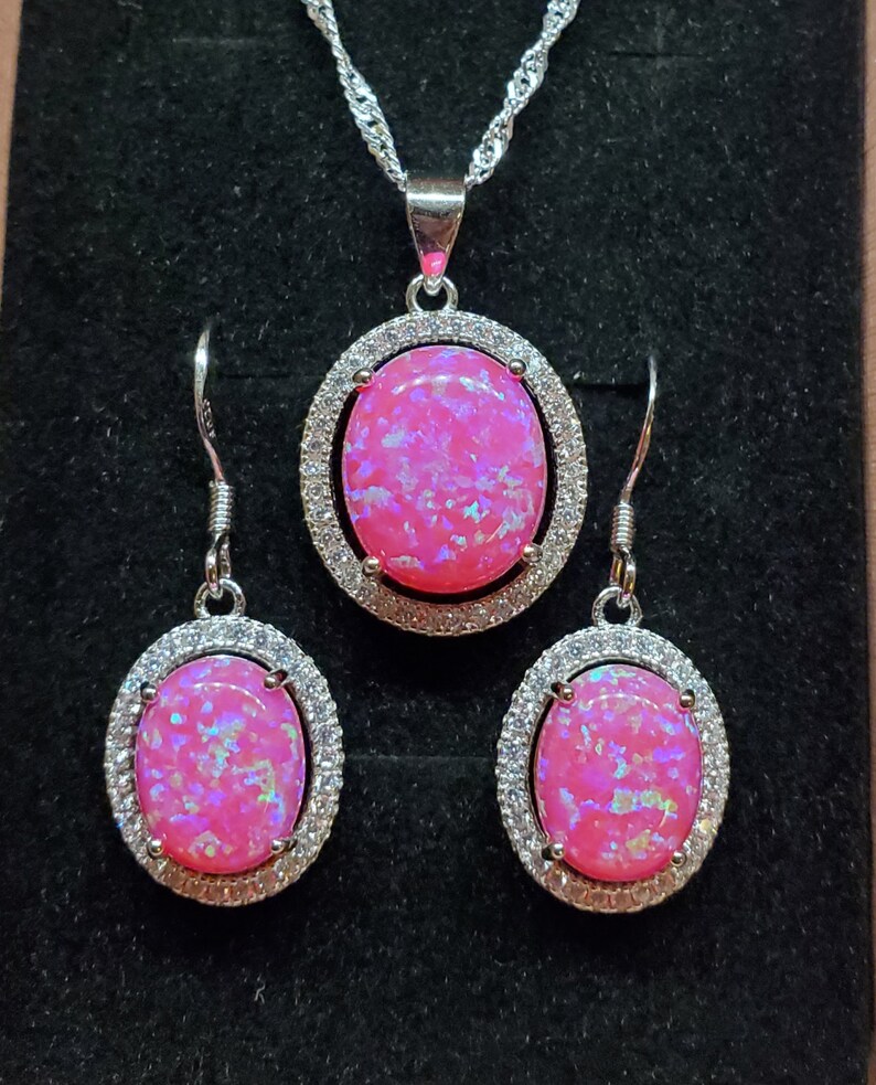 Puede incluir: Un conjunto de collar y pendientes de &oacute;palo rosa con una cadena de plata y piedras de forma ovalada rodeadas de circonitas c&uacute;bicas transparentes.
