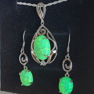 May include: A silver necklace and earrings set with a green opal pendant and matching earrings. The pendant is set in a delicate silver filigree design.