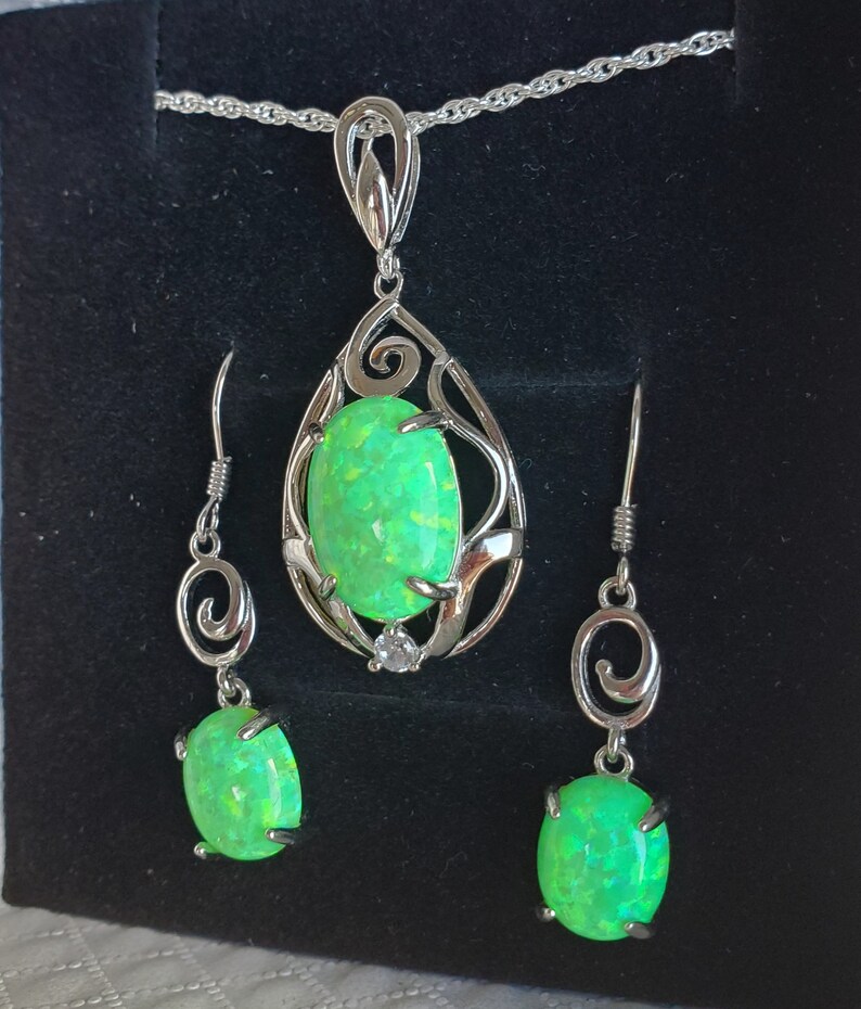 May include: A silver necklace and earrings set with a green opal pendant and matching earrings. The pendant is set in a delicate silver filigree design.