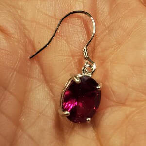 Puede incluir: Un pendiente de plata con una piedra preciosa de color rojo rub&iacute; de forma ovalada.