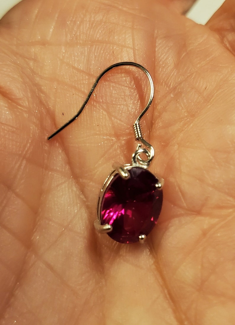Puede incluir: Un pendiente de plata con una piedra preciosa de color rojo rub&iacute; de forma ovalada.