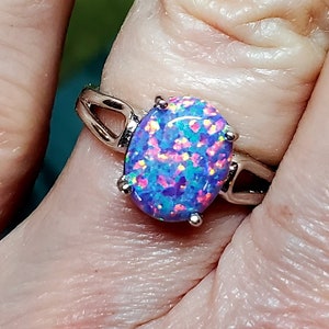May include: A silver ring with a large oval-shaped opal gemstone. The opal is a vibrant purple with flashes of pink, blue, and green.