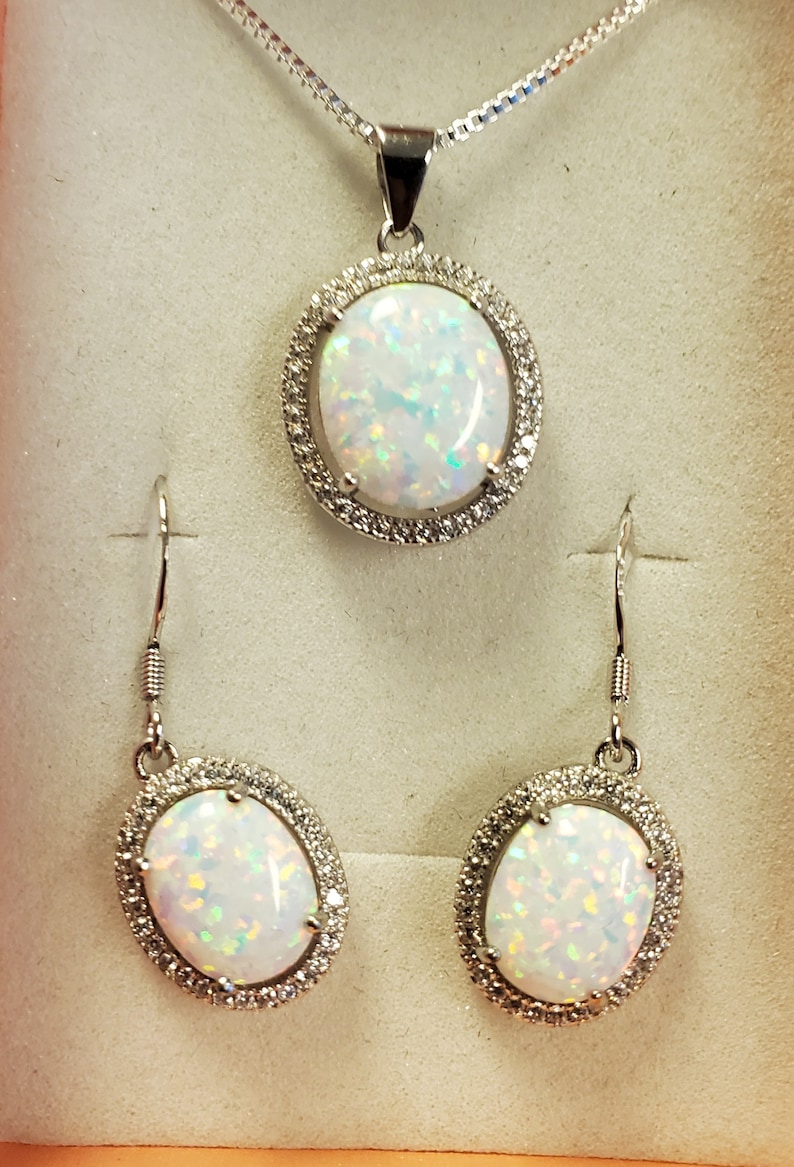 May include: A silver necklace and earrings set with oval-shaped white opal stones surrounded by a halo of smaller clear stones.
