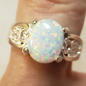 May include: A silver ring with a white opal gemstone. The ring has a delicate, ornate design.