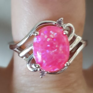 May include: A silver ring with a pink oval-shaped opal gemstone and small clear accent stones.