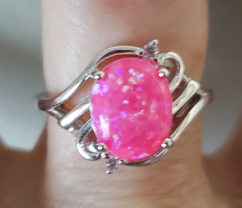 May include: A silver ring with a pink oval-shaped opal gemstone and small clear accent stones.