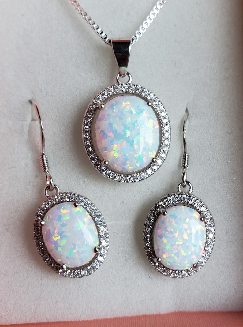 May include: A silver necklace and earrings set with oval-shaped white opal stones surrounded by a halo of clear cubic zirconia stones.