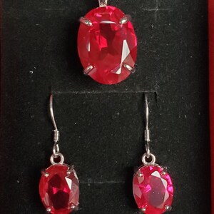 Puede incluir: Un conjunto de collar y pendientes de plata con un gran colgante de piedra roja ovalada y pendientes a juego.