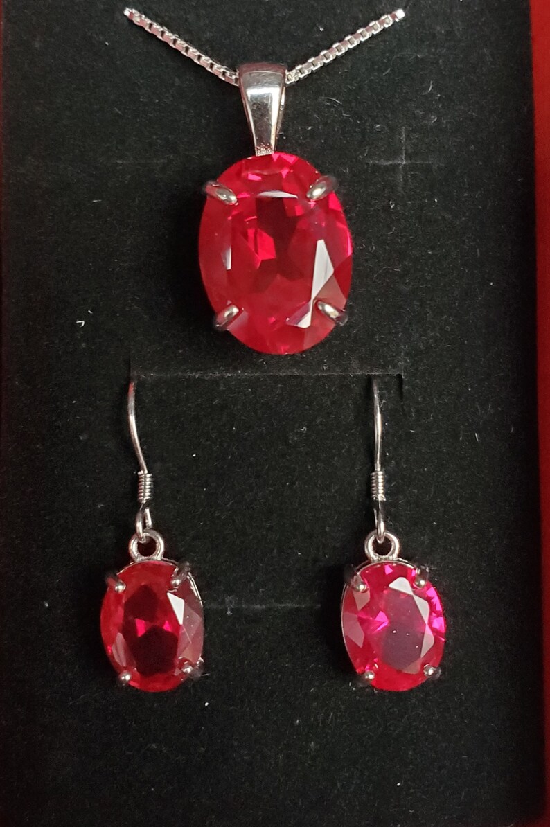 Puede incluir: Un conjunto de collar y pendientes de plata con un gran colgante de piedra roja ovalada y pendientes a juego.