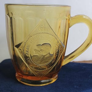 TAZA DE CORONACIÓN DE VIDRIO ÁMBAR con silueta en relieve del rey Jorge VI y la reina Isabel