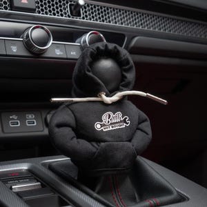 May include: Black hooded figure gear shift knob with white text that reads "Built Not Bought" and a wrench graphic.
