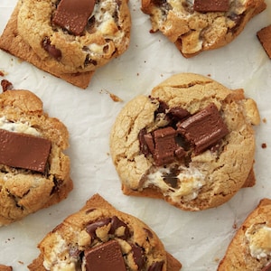 May include: A close-up of a baking sheet with nine s'mores cookies. The cookies are golden brown and have melted marshmallows and chocolate squares on top.