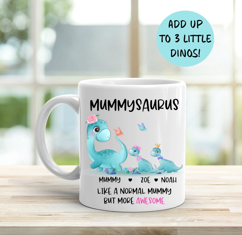 May include: White ceramic mug featuring a blue dinosaur illustration with the text "Mummyosaurus" and "Like a normal mummy but more awesome". The dinosaur has a pink flower crown and is holding a butterfly. Two smaller dinosaurs are behind the larger dinosaur. The text "Mummy", "Zoe", and "Noah" are below the dinosaurs.