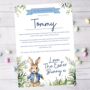 Op de afbeelding: Een blauwe en witte kaart met een cartoon konijn dat een blauw denim jack draagt. De kaart zegt "EGG-STRA SPECIAL DELIVERY" en "FOR THE ATTENTION OF: Tommy". De kaart heeft een bericht van de paashaas.