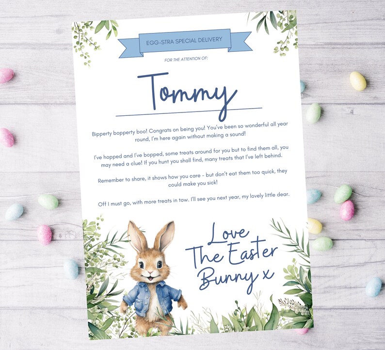 Op de afbeelding: Een blauwe en witte kaart met een cartoon konijn dat een blauw denim jack draagt. De kaart zegt "EGG-STRA SPECIAL DELIVERY" en "FOR THE ATTENTION OF: Tommy". De kaart heeft een bericht van de paashaas.