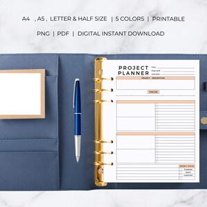 May include: A white printable project planner with sections for title, start date, due date, project description, timeline, and project status. The planner is open in a blue binder with gold rings.