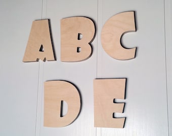 May include: Wooden letters spelling out the word "ABCDE" in a simple, blocky font. The letters are painted a light brown color and are arranged in a line on a white background.