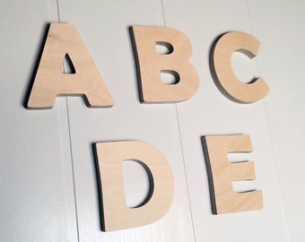 May include: Wooden letters spelling out the word "ABCDE" in a light brown color. The letters are arranged in a row on a white background.