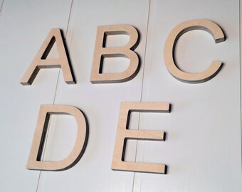 May include: Five wooden letters, A, B, C, D, and E, are arranged in a row on a white wood panel background. The letters are cut out of wood and have a natural wood color.