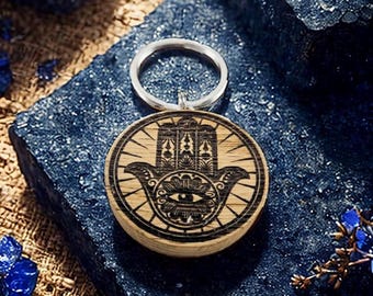 May include: A wooden keychain with a black and white hamsa hand design. The hamsa hand is a symbol of protection and good luck. The keychain is attached to a silver ring.