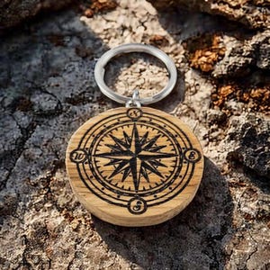 May include: A wooden compass keyring with a black compass design and a silver key ring. The compass features the cardinal directions N, S, E, and W.