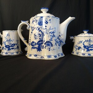 Op de afbeelding: Een blauwe en witte porseleinen theepot, roomkan en suikerpot set met een bloemenmotief.