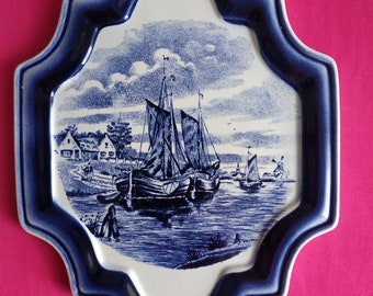 May include: A blue and white ceramic tile with a Dutch scene of a sailboat on a canal with houses in the background.