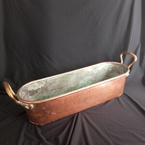 May include: A large, oval-shaped copper planter with two brass handles. The planter has a worn, aged patina and is perfect for displaying plants or flowers.