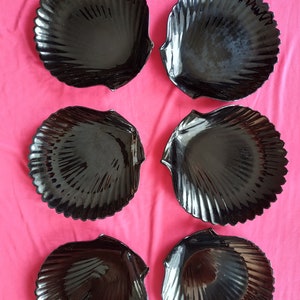 Könnte beinhalten: Sechs schwarze, keramik-gefertigte Schalen in Muschelform. Die Schalen sind in zwei Reihen mit je drei Schalen angeordnet, wobei die obere Reihe leicht versetzt zur unteren Reihe ist.