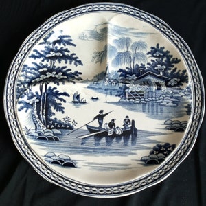 May include: A white ceramic divided plate with a blue and white design of a river scene with trees, a house, and a boat with people in it.