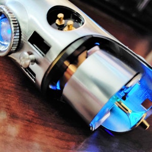 Puede incluir: Primer plano de una empu&ntilde;adura de sable l&aacute;ser plateada con una luz azul que emana del extremo. La empu&ntilde;adura tiene un pomo plateado y un anillo negro alrededor del medio.