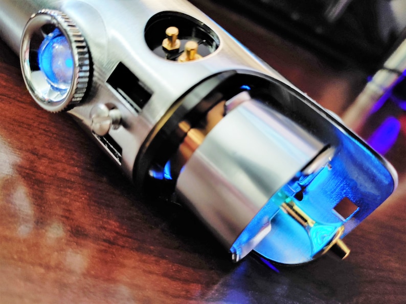 Puede incluir: Primer plano de una empu&ntilde;adura de sable l&aacute;ser plateada con una luz azul que emana del extremo. La empu&ntilde;adura tiene un pomo plateado y un anillo negro alrededor del medio.