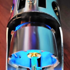 Puede incluir: Primer plano de una empu&ntilde;adura de sable de luz plateada con una luz azul que emana del extremo. La empu&ntilde;adura tiene un peque&ntilde;o pomo redondo plateado en la parte superior.