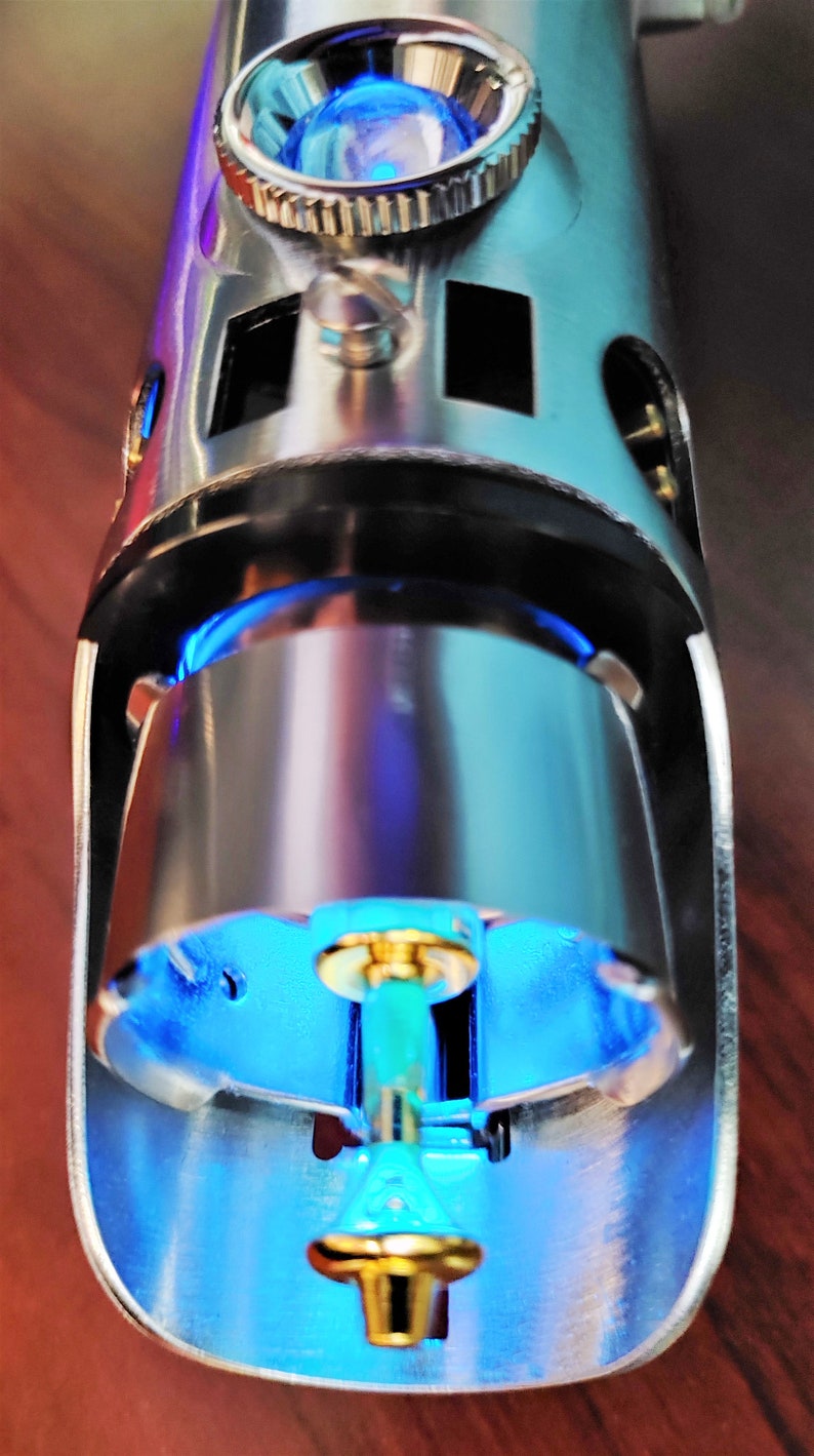 Puede incluir: Primer plano de una empu&ntilde;adura de sable de luz plateada con una luz azul que emana del extremo. La empu&ntilde;adura tiene un peque&ntilde;o pomo redondo plateado en la parte superior.