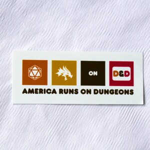 Könnte beinhalten: Ein weißer Aufkleber mit vier farbigen Quadraten. Die Quadrate zeigen einen 20-seitigen Würfel, einen Drachen, das Wort "ON" und die Buchstaben "D&D". Der Aufkleber lautet "America Runs on Dungeons".