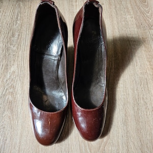 Peut inclure: Une paire d'escarpins en cuir verni bordeaux foncé avec un bout arrondi et un talon haut. L'intérieur des chaussures est doublé de cuir marron foncé, et la marque Gucci est embossée sur la zone du talon à l'intérieur de la semelle.