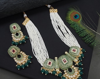 May include: An ornate necklace and earring set. The necklace features multiple strands of white beads, connected to green and gold pendants with red accents. The earrings mirror the pendant design, with green beads and gold detailing.