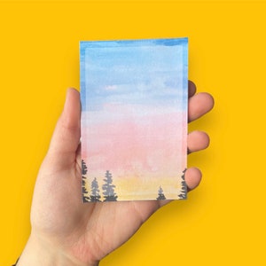 May include: A watercolor painting of a pink and blue sunset over a forest of dark green trees. The sky is a gradient of light blue, pink, and yellow.