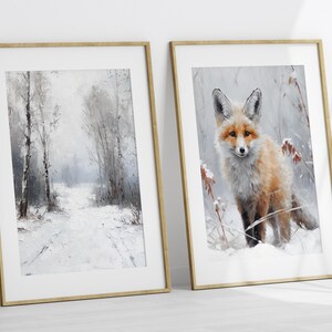 May include: Two framed prints, one depicting a snowy forest path and the other featuring a red fox standing in a snowy woodland. Both prints have a white background and a light wood frame.