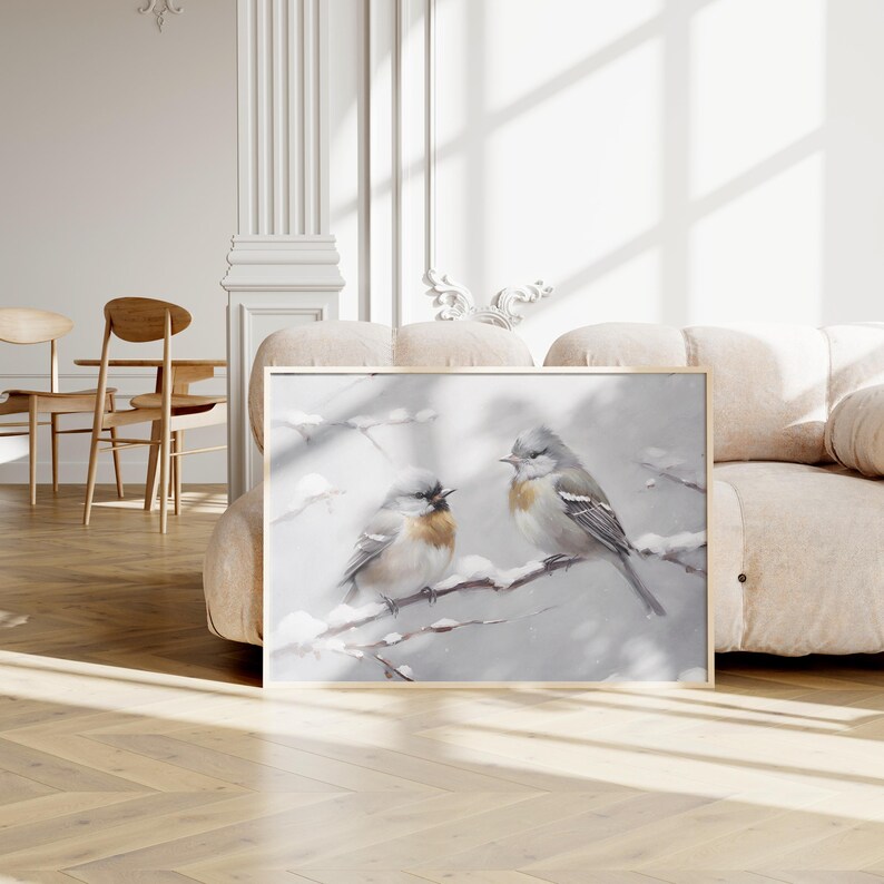 May include: A framed painting depicting two birds perched on a snowy branch. The birds are grey and white with brown accents. The background is a soft grey with a subtle snow effect.