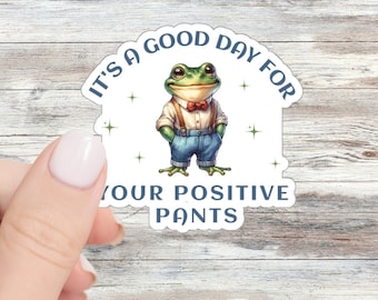 May include: A die-cut sticker featuring a green frog wearing a white button-down shirt, a red bow tie, and blue denim overalls. The text IT'S A GOOD DAY FOR YOUR POSITIVE PANTS is printed in dark blue capital letters around the central frog illustration.