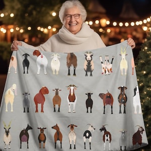 May include: A gray fleece blanket with a pattern of various goats in different poses. The goats are in various colors, including white, brown, black, and tan. The blanket is held by a person in the background.