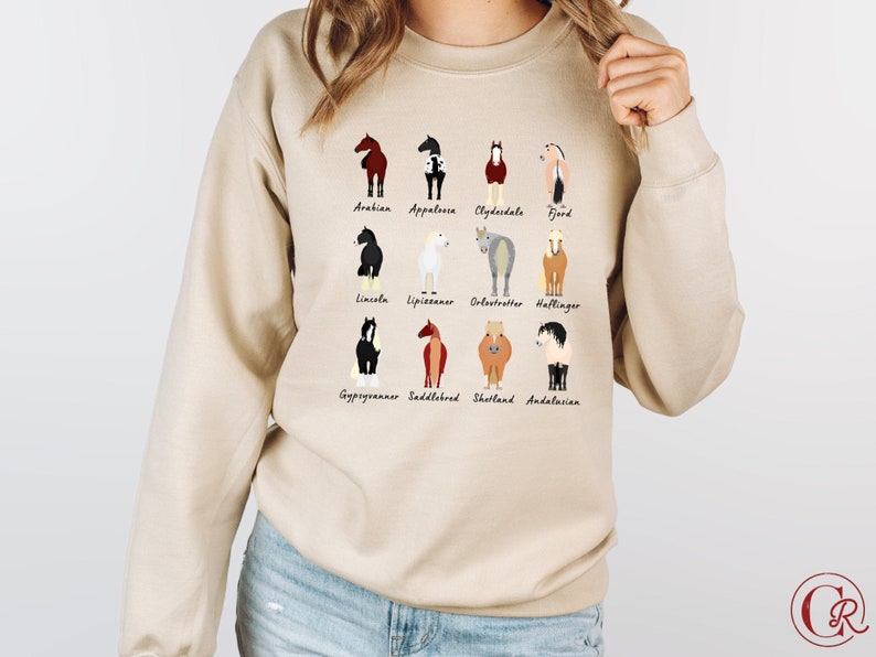 K&ouml;nnte beinhalten: Beigefarbener Pullover mit einer Grafik verschiedener Pferderassen, darunter Araber, Appaloosa, Clydesdale, Fjord, Lincoln, Lipizzaner, Oldenburg, Haflinger, Gypsy Vanner, Saddlebred, Shetland und Andalusier.