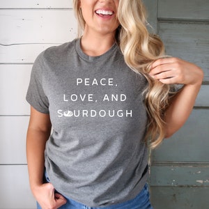 Pode incluir: Uma camiseta cinza com o texto "Peace, Love, and Sourdough" impresso em branco.