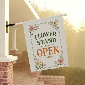 May include: A rectangular off-white garden flag featuring the dark green text FLOWER STAND and the orange text OPEN. The design is framed by a thin green border and decorated with colorful floral illustrations in the four corners of the flag.