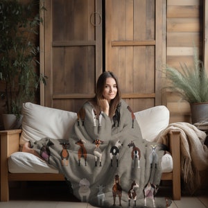 May include: A woman sits on a white sofa wrapped in a grey fleece throw blanket with a pattern of brown, white and black goats.