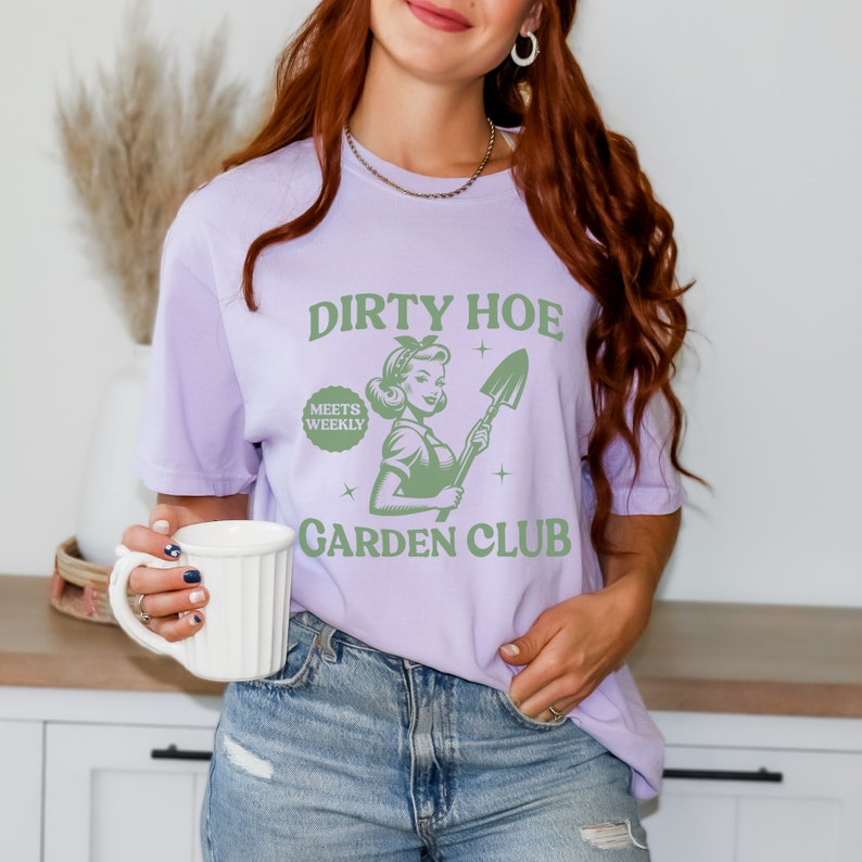 May include: A purple t-shirt with the text "Dirty Hoe Meets Weekly Garden Club" and a green illustration of a woman holding a shovel.