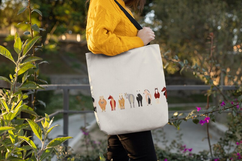 May include: A white tote bag with a black strap and a row of colourful horses printed on the front. The horses are facing away from the viewer.