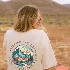 May include: Ivory t-shirt with a graphic of mountains and the text "Sometimes you just need to change your altitude".