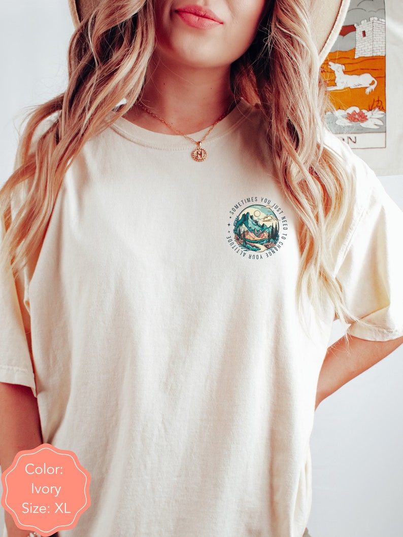May include: Ivory t-shirt with a graphic of mountains and a river with the text "Sometimes you just need to change your attitude".